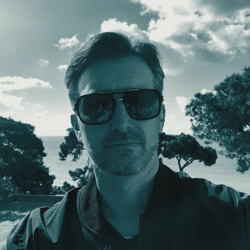 Patrizio con gli occhiali da sole, davanti al mare e ai pini